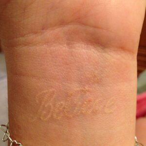 Healed white text tattoo.